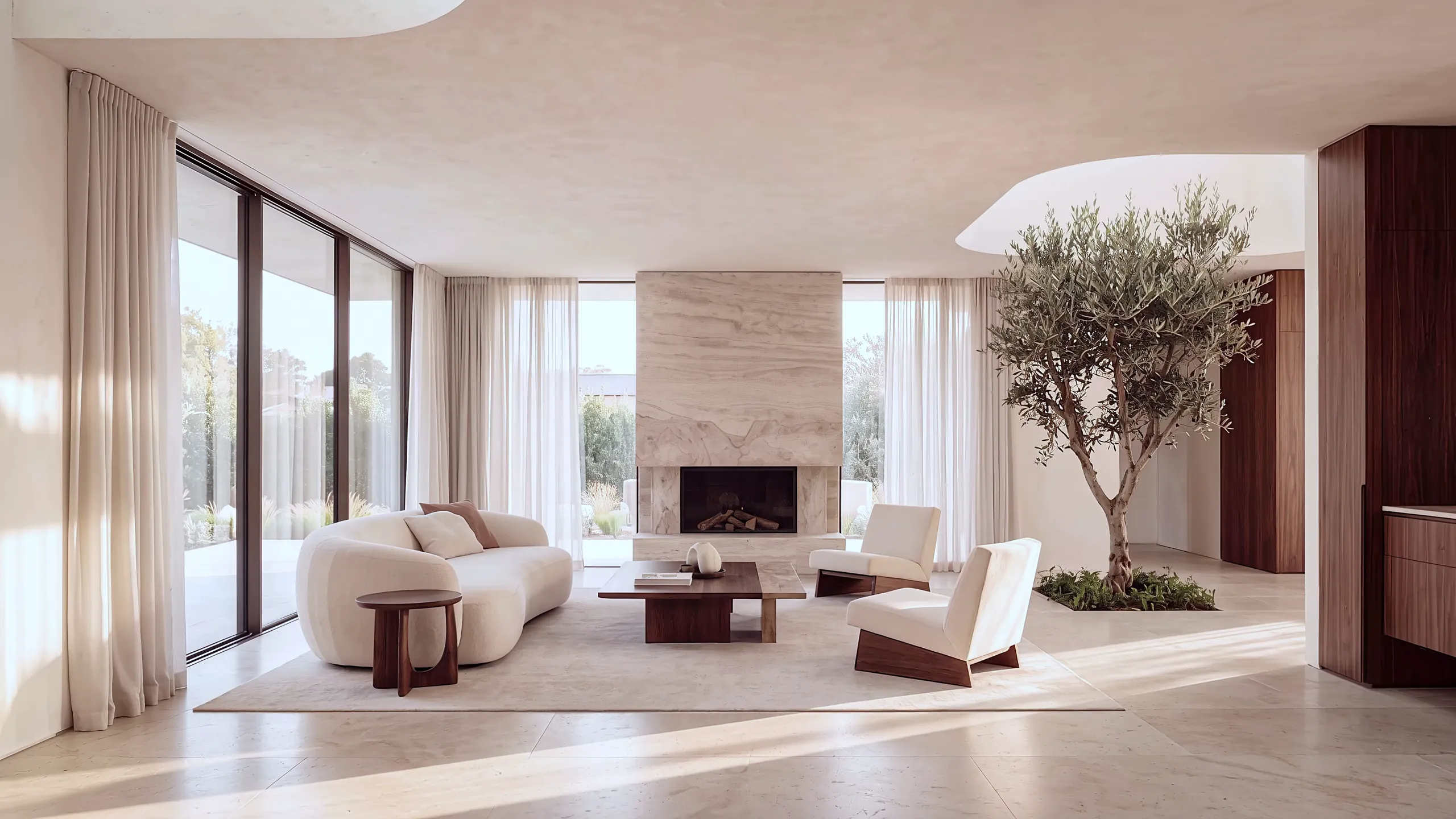 A living room with a travertine fireplace, curved sofa and an indoor olive tree
